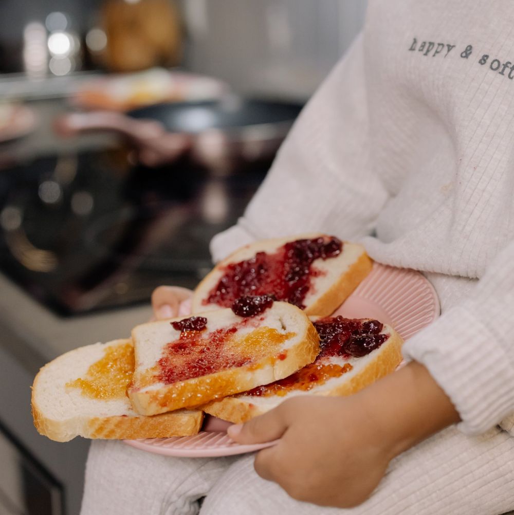 Child holding a pink plate of toast with jam